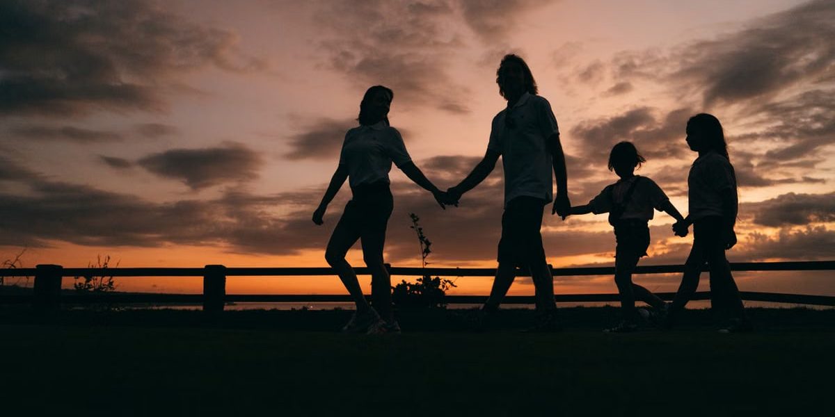 A family walks hand in hand against a vibrant sunset, evoking togetherness and peace.