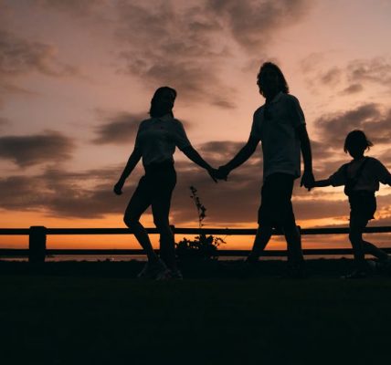 A family walks hand in hand against a vibrant sunset, evoking togetherness and peace.