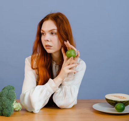Caucasian woman sitting at table holding lime with broccoli and melon.